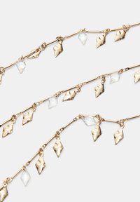 Collana delicata in oro con pendenti metallici irregolari e testurizzati e accenti di cristallo trasparente, che mostra un design elegante e stratificato.