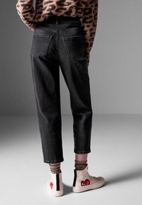 Mustat farkut, joissa on korkea vyötärö ja kapenevat lahkeet, yhdistettynä vaaleanvärisiin tennareihin, joissa on punainen sydänkuvio ja vetoketjut.