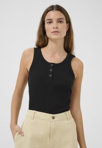 Top in cotone nero a coste con scollatura rotonda e patta con tre bottoni. Il tessuto è morbido e ha una forma aderente. Abbinato a pantaloni beige a vita alta.