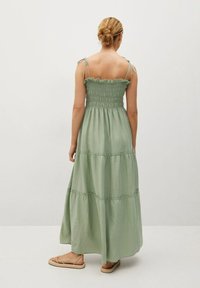 Robe maxi en tissu vert doux, avec un corsage à smocks, des bords froncés, des bretelles fines et un design de jupe à volants.