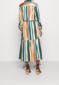 Abito lungo multicolore con strisce verticali in teal, marrone e crema. Presenta una gonna a strati e maniche lunghe con polsini a bottone.