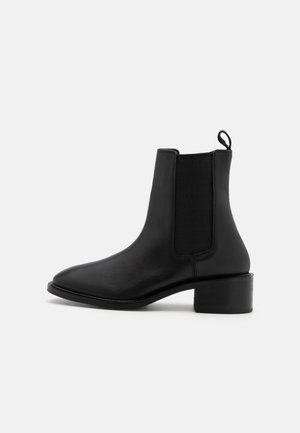 Bottes chelsea en cuir noir avec des panneaux élastiques sur les côtés, bout arrondi et un talon block de 5 cm ; elles disposent d'une languette à l'arrière.