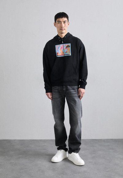 Black hoodie with a colorful graphic on the front, paired with grey jeans and white sneakers. Soft fabric and relaxed fit.