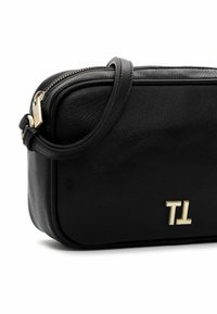 Sort læder crossbody taske med gyldent lynlås og "TL" gyldent logo foran, med justerbar rem, der er snoet over toppen.