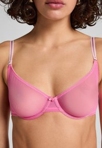 Pink sheer bra with underwire, lace trim, and adjustable straps. Features a decorative rose detail at the center. Smooth texture.