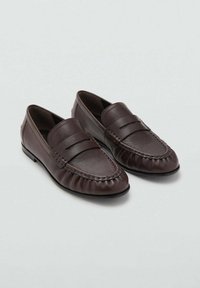 Mocasines de cuero marrón con punta redondeada, que presentan costuras decorativas y un acabado suave. Una banda elevada en la parte superior añade detalle.