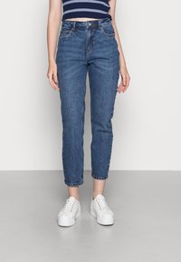 Blå denimjeans med hög midja, rak passform, och kort längd samt subtila blekningar; ihop med vita sneakers för kontrast.