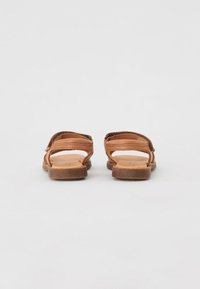 Bruine leren sandalen met een open teen ontwerp, met twee verstelbare banden en een platte zool met een subtiele textuur.