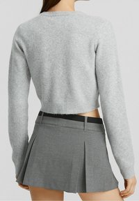 Maglione grigio corto con una consistenza morbida e orlo a coste abbinato a una gonna plissettata grigia con una vita nera.