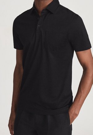 Polo noir en coton, avec un col, trois boutons et une poche poitrine. Manches courtes avec une coupe ajustée.