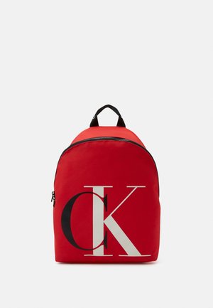 Rode stoffen rugzak met een afgeronde vorm, voorzien van een groot zwart-wit "CK"-logo, ritssluiting en een zwart handvat bovenop.