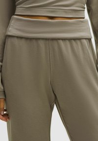 Szürke, puha anyagú joggerek széles, hajtott derékkal és laza fit-tel. Jellemzője a texturált felület, oldalsó zsebek és a cuffolt szegélyek.