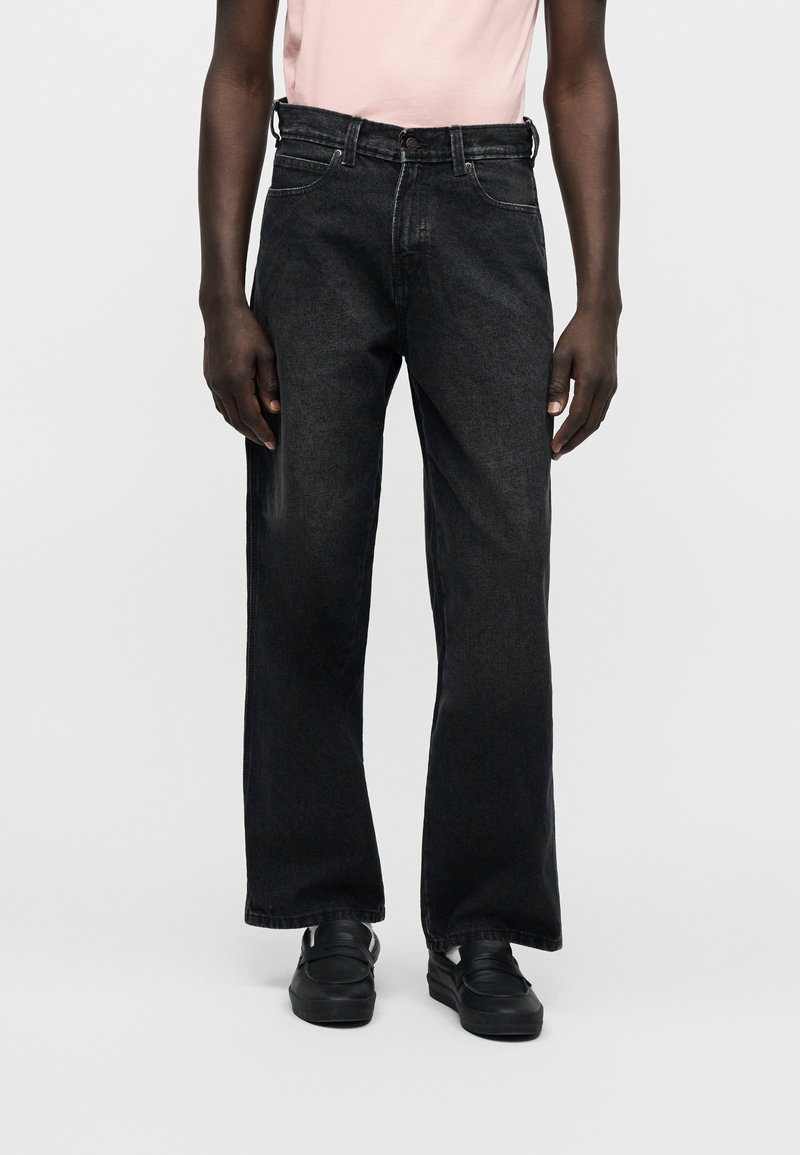 Zwarte jeans met wijde pijpen van denim, met een hoge taille, riemlussen, voorzakken en een donkere wassing, gedragen met zwarte schoenen.