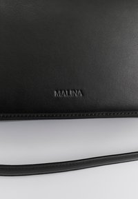 Μαύρη δερμάτινη τσάντα χειρός με υφή στην επιφάνεια, που φέρει ανάγλυφο λογότυπο "MALINA". Περιλαμβάνει λεπτό λουράκι ώμου και καθαρές ραφές.