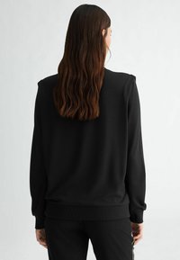 Felpa nera con vestibilità rilassata, polsini a costine e texture liscia, progettata con dettagli sulle spalle, mostrata da dietro.