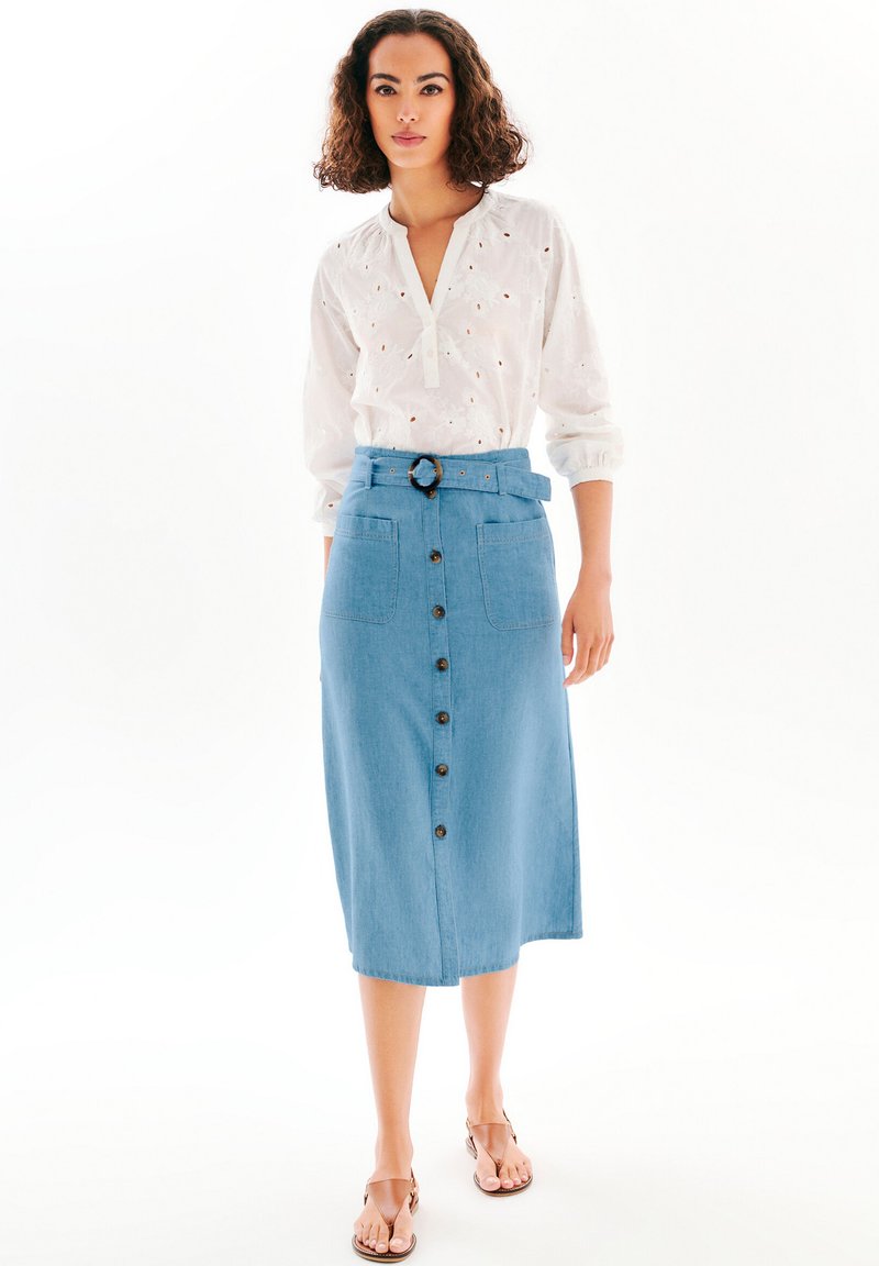 Lätt vit blus med broderier och v-ringning, kombinerad med en högmidjad blå denimkjol med knappar och bälte i midjan.