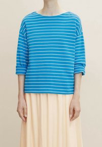 T-shirt a righe blu e bianche, collo rotondo, maniche 3/4, tessuto morbido, vestibilità leggermente ampia, abbinato a una gonna leggera e fluida.