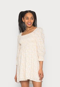 Vestido floral com decote quadrado, mangas bufantes e corpete franzido. O tecido leve apresenta pequenas flores laranja e azuis sobre um fundo branco.