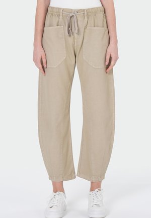 Beige Freizeithose mit elastischem Bund und Kordelzug, großen Fronttaschen, getragen mit weißen Sneakers.