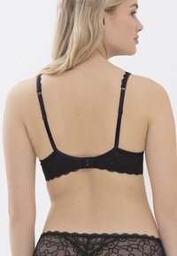 Zwarte kant bralette met geschulpte randen, verstelbare bandjes en een haak-en-oogsluiting aan de achterkant. Geweven bloemenpatroon door het hele ontwerp.