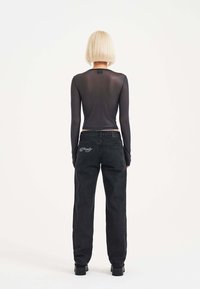 Long-sleeve black sheer top paired with high-waisted black denim jeans featuring embroidered detail on the back pocket. Smooth texture.