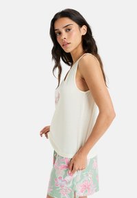 Hellbeiges Tanktop mit V-Ausschnitt, verziert mit pastelblumenförmiger Stickerei. Kombiniert mit mintgrünen Shorts, geschmückt mit rosa Blumenmustern.