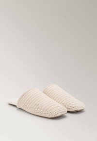 Pantofole beige lavorate a maglia con un design testurizzato a coste e schienale aperto, dotate di una punta arrotondata e una suola piatta. Materiale morbido e accogliente.