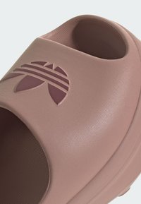 Roze instapklomp van textuur materiaal, met een prominent logo met gebogen lijnen en een circulair element op de bovenkant.