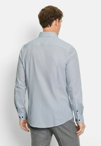 Langärmliges Hemd mit Kragen in blauem Muster, das kleine dunkelblaue Punkte auf hellem Hintergrund zeigt und schwarze Knopfakzente an den Manschetten hat.
