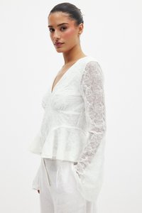 Weiße Peplum-Bluse mit langen, transparenten Ärmeln, die mit floralem Stickerei verziert ist und über einen V-Ausschnitt verfügt. Weicher Stoff und leichtes Material.