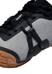 Chaussure de sport noire et argentée avec une tige texturée, des lacets noirs et une semelle en caoutchouc. Les détails notables incluent un design en toile d'araignée et un patch de logo.