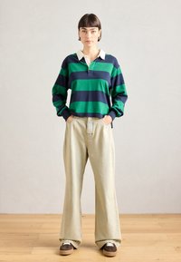 Gestreepte lange mouwen polo met groene en marineblauwe horizontale strepen, witte kraag; gecombineerd met beige wijde broek en bruine sneakers.