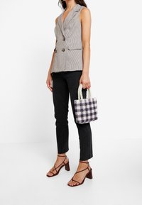 Grå hundtandsmönstrad ärmlös blazer, svarta skinny jeans och en liten, vävd lila och vit rutig handväska med pärlhandtag. Bruna remsandaler.