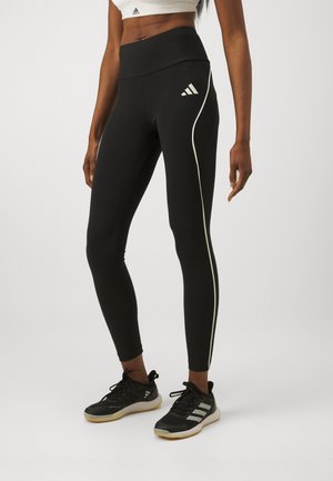 Leggings noirs avec une taille haute, ornés d'une bande latérale blanche contrastante et d'un logo Adidas sur la hanche. Fabriqués en matériau extensible.