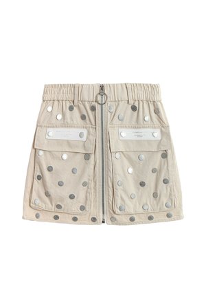 Minifalda beige con cremallera frontal, dos grandes bolsillos con solapa, cinturilla elástica y tachuelas circulares plateadas dispersas por la tela.