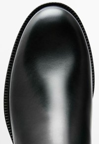 Schwarze Leder-Stiefelette mit einer runden Zehe, glatter Textur und rutschfester Sohle für besseren Halt. Minimalistisches Design ohne zusätzliche Verzierungen.