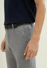 Grijze geweven broek met een slim fit, gecombineerd met een zwarte riem. De outfit wordt aangevuld met een marineblauw poloshirt.