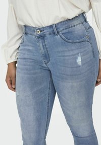 Svetlomodré džínsové nohavice s priliehavým strihom, s poškodenou aplikáciou a klasickým piatimi vreckami. Vyrobené z pružného materiálu.