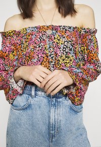Zwart off-the-shoulder blouse met meerkleurige bloemenpatronen, ruches aan de mouwen en een losse fit, gecombineerd met hoge, blauwe denim shorts.