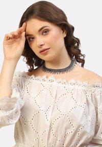 Sort metal choker halskæde med indviklede s�ølvfarvede detaljer og hængende dekorative elementer. Båret af en model med bølget hår.