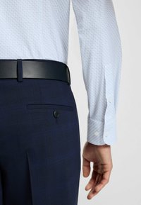 Camicia a maniche lunghe in tessuto blu chiaro con un piccolo motivo circolare, abbinata a pantaloni blu scuro su misura con una tasca posteriore con bottone.