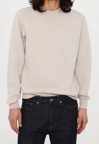 Jasnobeżowa bluza z okrągłym dekoltem, ściągaczami przy mankietach i u dołu. Na piersi znajduje się drobny biały napis. Połączona z ciemnymi jeansami.