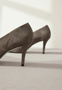Des escarpins en daim gris avec un talon aiguille de 10 cm et une pointe fine. Les chaussures présentent une texture lisse et une légère brillance.