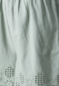 Tissu blanc avec des motifs découpés géométriques brodés le long du bord inférieur et de subtils plis verticaux.