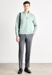 Φούστα σε μέντα πράσινο χρώμα με φερμουάρ, ελαφρύ ύφασμα, ριμπ μανσέτες, σε συνδυασμό με γκρι ραμμένο παντελόνι και μαύρα loafers, σε ουδέτερο φόντο.