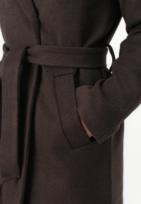 Brown wool coat with a belt, featuring a patch pocket and wide sleeves. The fabric has a soft texture and a subtle sheen.