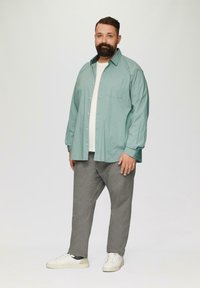 Jasny turkusowy koszula z guzikami z małymi ciemnymi wzorami, założona na białą koszulkę, w połączeniu z szarymi spodniami i białymi trampkami.