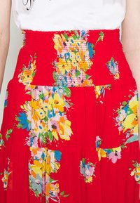 Rotes Blumenkleid mit einem gerafften Taillenbund, das leuchtend gelbe, rosa, blaue und grüne Blumenmuster aufweist, sowie einen fließenden, plissierten Rock.