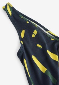 Gros plan d'un tissu sombre avec des formes abstraites jaunes et vertes montrant l'épaule et l'encolure d'un vêtement sans manches.