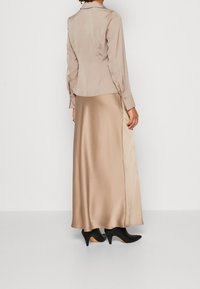 Beige satinblus med lång ärm och krage, tillsammans med en matchande golvlängd satinkjol. Svarta pumps med spetsig tå.